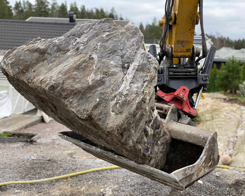 Grävmaskin med sten i grävskopan.